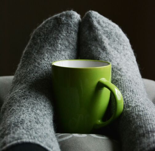 feet in warm socks with a green mug held between them to keep warm