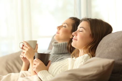 women sat holding mugs leant back on a sofa
