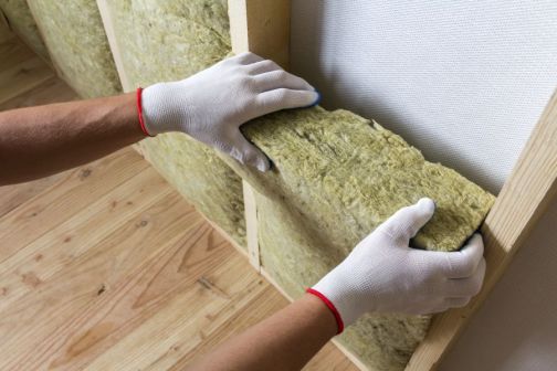 home insulation being installed in a wall by a pair of gloved hands