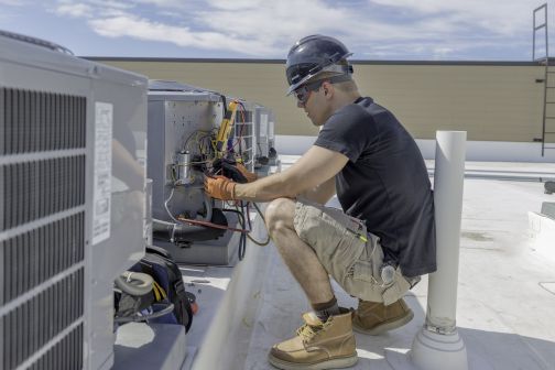 Tradesman repairing fan coil on roof of building