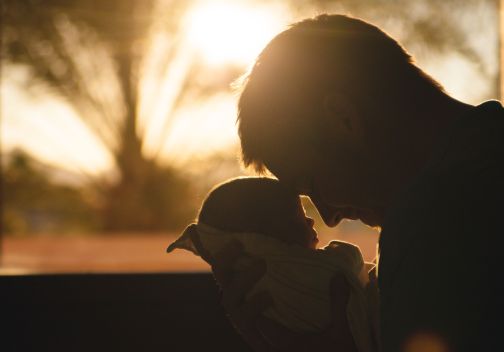 father with baby placing foreheads against each other sunset in background