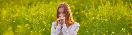 woman sneezing stood in field of wild flowers
