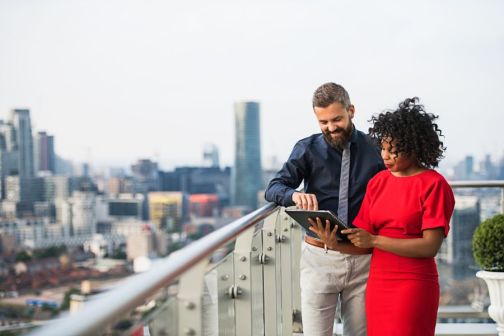 man and woman looking at notebook on a balcony with cityscape in background