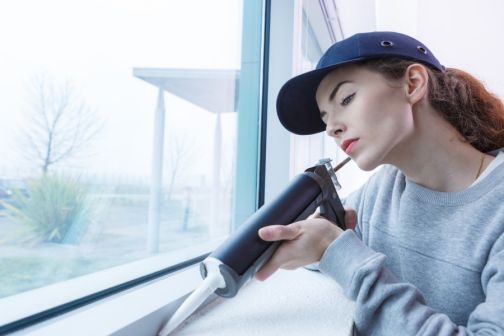 woman sealing drafty window gaps