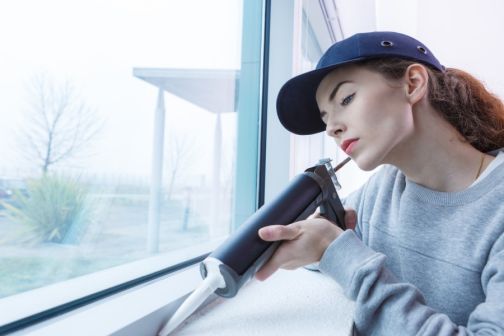 woman sealing drafty window gaps 